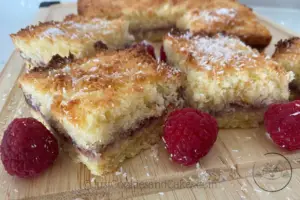 Raspberry Coconut slice on board with fresh raspberries